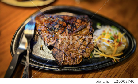 juicy grilled T bone steak, perfectly seared, served alongside a loaded baked mash potato on a warmly lit rustic dining setup. Ideal for culinary content juicy grilled T bone steak, perfectly seared, served alongside a loaded baked mash potato on a warmly lit rustic dining setup. Ideal for culinary content 129005740