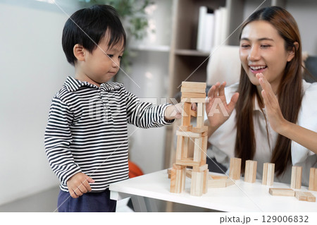 Child Development. Engaging toddler stacking wooden blocks with caregiver in a cozy indoor setting. Child Development. Engaging toddler stacking wooden blocks with caregiver in a cozy indoor setting. 129006832