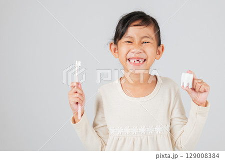 Dentist shows kid girl how to brush tooth model after tooth loss. Asian child smiles with gap, holding toothbrush, learning dental care and healthy teeth habits. isolated white background Dentist shows kid girl how to brush tooth model after tooth loss. Asian child smiles with gap, holding toothbrush, learning dental care and healthy teeth habits. isolated white background 129008384