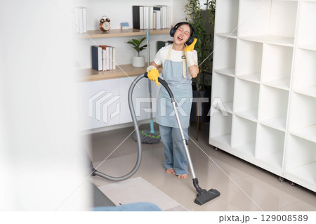 Home Cleaning. Happy woman dancing while vacuuming in a stylish living space. Home Cleaning. Happy woman dancing while vacuuming in a stylish living space. 129008589