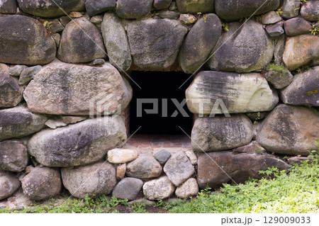 Stone Wall with Small Square Opening and Green Vegetation Surrounding It 129009033