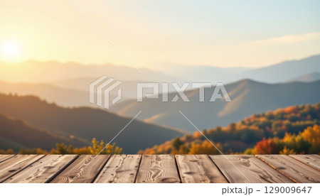 Sunset over mountain range with wooden table in foreground and colorful autumn trees in soft light 129009647