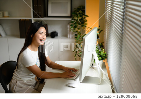 Smiling young woman sitting at a desk and working on a desktop computer 129009668
