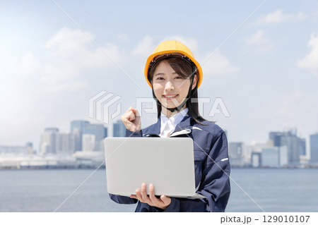 ノートパソコンを使いガッツポーズをする作業服を着た若い女性 129010107