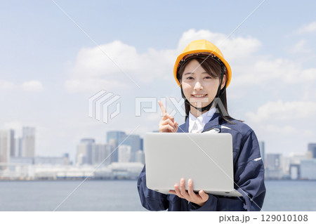 ノートパソコンを使い指差しをする作業服を着た若い女性 ノートパソコンを使い指差しをする作業服を着た若い女性 129010108