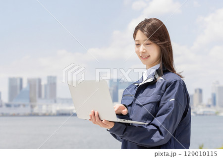 ノートパソコンで検索をする作業服を着た若い女性（建築・建設・土木・物流・産業） 129010115