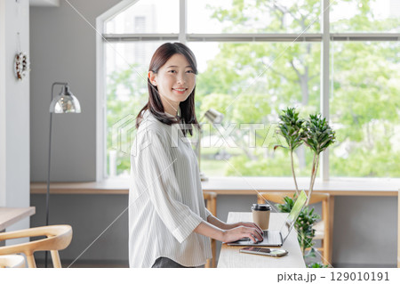 コワーキングスペースで立ちながらノートパソコンを使う女性 129010191