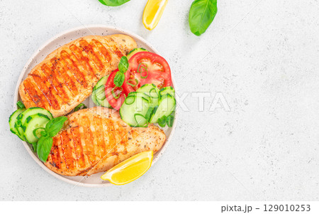 Grilled chicken breast with fresh vegetables and lemon on white plate. top view. copy space 129010253