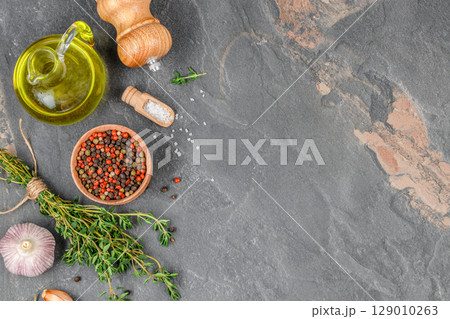 Cooking ingredients including olive oil, garlic, herbs, salt, and pepper on a dark stone kitchen surface. top view. copy space. 129010263