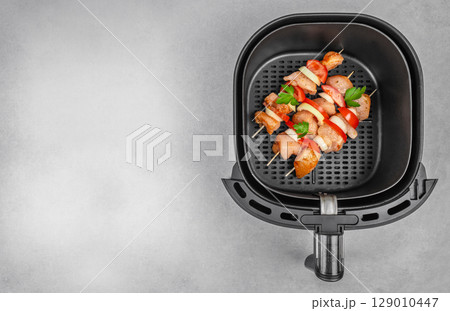 Raw chicken skewers with vegetables in an air fryer basket, ready for cooking. copy space, top view Raw chicken skewers with vegetables in an air fryer basket, ready for cooking. copy space, top view 129010447
