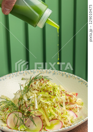 Fresh green dressing is delicately drizzled over a vibrant cabbage and radish salad, garnished with dill and flax seeds in a patterned bowl Fresh green dressing is delicately drizzled over a vibrant cabbage and radish salad, garnished with dill and flax seeds in a patterned bowl 129010475