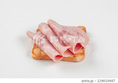 Toasted bread topped with rolled slices of luncheon meat on a white background Toasted bread topped with rolled slices of luncheon meat on a white background 129010487