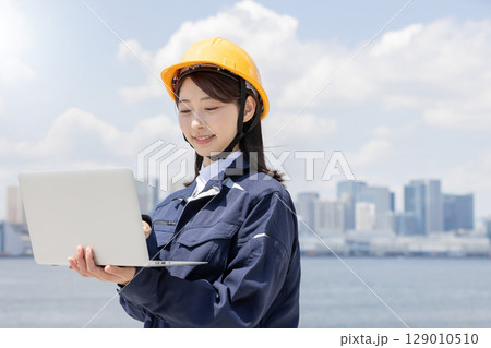 ノートパソコンを使う作業服を着た若い女性 129010510