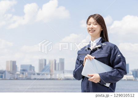 見上げる作業服を着た若い女性（建築・建設・土木・物流・産業） 129010512