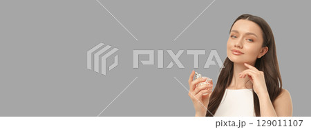 Woman in white dress holds perfume bottle confidently in studio Woman in white dress holds perfume bottle confidently in studio 129011107