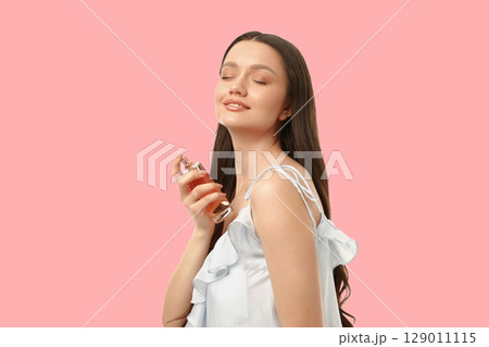 Woman smiles while applying perfume with closed eyes 129011115