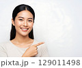 Radiant Asian woman with a welcoming smile pointing to blank copy space. 129011498