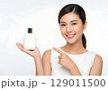 Radiant Asian Woman with Flawless Skin Joyfully Presents a White Cosmetic Bottle. 129011500