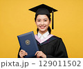 Radiant Graduates Joyful Portrait Holding Diploma Against a Bold Yellow Background. 129011502