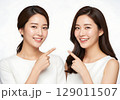 Two Radiant Asian Women with Perfect Smiles Pointing Inward on White. 129011507