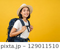 Adventurous Young Asian Woman with Backpack Smiles Cheerfully Against a Bold Yellow Background. 129011510