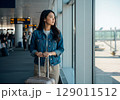Awaiting Departure Pensive Woman with Luggage Gazes Out Airport Terminal Window. 129011512