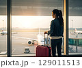 Awaiting Departure Woman with Red Luggage Gazes at Tarmac at Dawn. 129011513