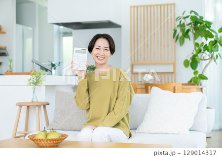 リビングで電卓を持つミドルの女性 リビングで電卓を持つミドルの女性 129014317