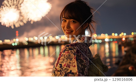 打ち上げ花火と夜の川辺を背景に笑顔の浴衣女性が振り返る瞬間 129016806