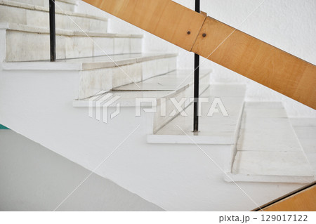 A flight of stairs with marble steps. Whitewashed walls and wooden staircase railings. The staircase of an old building. A flight of stairs with marble steps. Whitewashed walls and wooden staircase railings. The staircase of an old building. 129017122