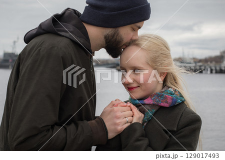 Bearded man and young blond woman couple hugging each other kissing at seaside Bearded man and young blond woman couple hugging each other kissing at seaside 129017493