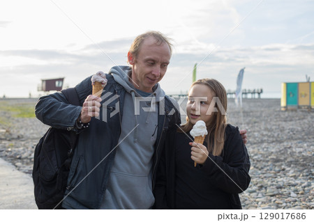 Happy child daughter and her father walking and eating ice cream outdoors. Happy family, childhood 129017686