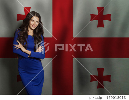 Cheerful young woman in blue dress smiling against Georgian flag background 129018018