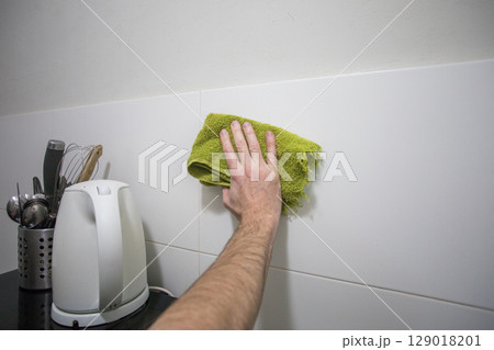 Hand with green rag cleaning white ceramic tile in kitchen 129018201