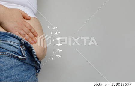 Female hand and belly close up on gray background. Weight loss and aesthetic surgery concept. Female hand and belly close up on gray background. Weight loss and aesthetic surgery concept. 129018577