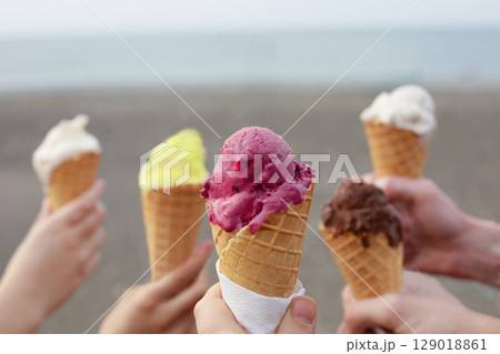 Many hands holding ice cream cones with different  scoops of ice cream on sea beach background.  129018861