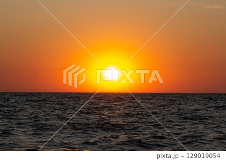 A vibrant sunset over the sea with warm colors reflecting on the gentle waves A vibrant sunset over the sea with warm colors reflecting on the gentle waves 129019054