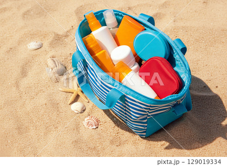 A beach-ready cosmetic bag overflowing with various sunscreens, moisturizers, and after-sun creams, all resting on golden sand. Perfect for highlighting sun protection essentials 129019334