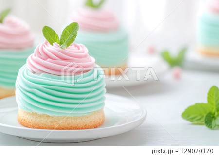 Delicate pastel cakes with turquoise and pink frosting adorned with fresh mint leaves on white plates Delicate pastel cakes with turquoise and pink frosting adorned with fresh mint leaves on white plates 129020120