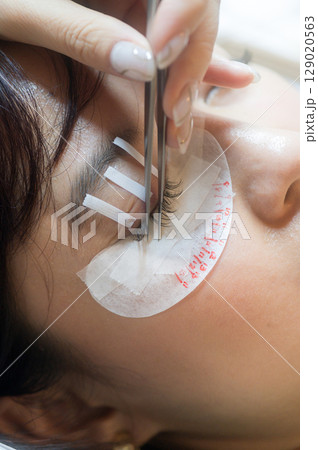 Young southeast asian woman undergoes an eyelashes extension procedure for natural beauty in salon. female focuses on health wellness and makeup for beautiful eyes 129020563