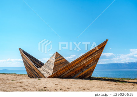 wooden boat sculpture on shore tranquil lake under clear sky in afternoon light. closeup. 129020619