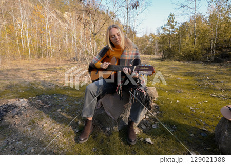 Beautiful blonde girl playing acoustic guitar and singing relaxing enjoying outdoors on sunny autumn day. Hippie woman in boho style learning and practicing playing musical instrument. Fall leaves Beautiful blonde girl playing acoustic guitar and singing relaxing enjoying outdoors on sunny autumn day. Hippie woman in boho style learning and practicing playing musical instrument. Fall leaves 129021388