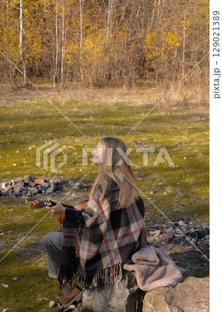 Blonde woman playing string guitar outdoors in autumn forest. Concept of sound therapy, mental health and wellness rituals. Calmness tranquility audio-sensory practices. Aura farming energy Blonde woman playing string guitar outdoors in autumn forest. Concept of sound therapy, mental health and wellness rituals. Calmness tranquility audio-sensory practices. Aura farming energy 129021389
