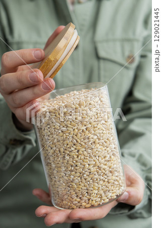 Unrecognizable woman holding refillable glass jar with raw pearl barley porridge. Refill product format eco-friendly living. Filling reusable container Whole spelt grain species. High protein fiber Unrecognizable woman holding refillable glass jar with raw pearl barley porridge. Refill product format eco-friendly living. Filling reusable container Whole spelt grain species. High protein fiber 129021445