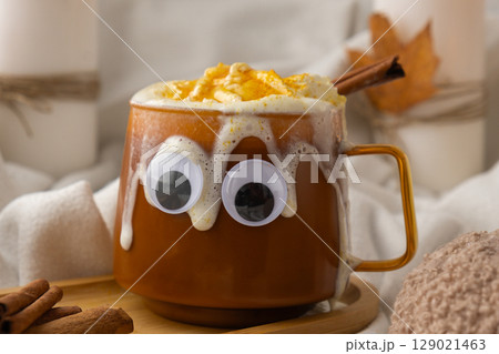 Seasonal drink cacao coffee with whipped cream and cinnamon sticks Halloween funny face on cup Hello Fall Halloween concept. Celebrating autumn holidays at cozy home on the windowsill atmosphere 129021463