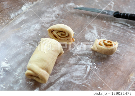 Dough, rolled into roll, is cut into slices for baking cinnamon buns 129021475