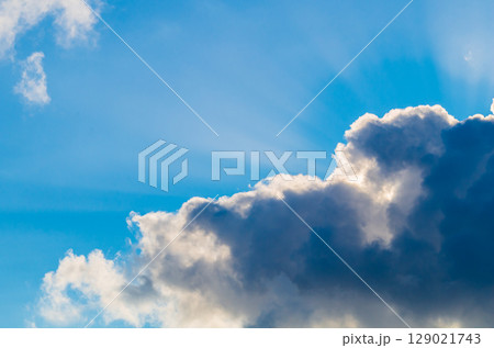 Photo of sky, in which sun is hidden behind dense rain clouds, shines through with its yellow glow in some places, and scattering rays are visible against background of blue sky and a white veil Photo of sky, in which sun is hidden behind dense rain clouds, shines through with its yellow glow in some places, and scattering rays are visible against background of blue sky and a white veil 129021743