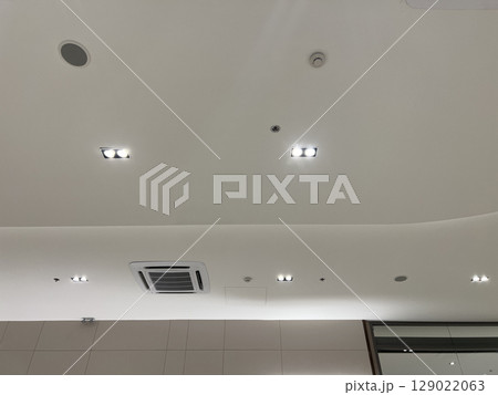 Functional and modern white ceiling with recessed lighting, air conditioner, security camera, smoke detector, and speaker creating secure and comfortable atmosphere Functional and modern white ceiling with recessed lighting, air conditioner, security camera, smoke detector, and speaker creating secure and comfortable atmosphere 129022063