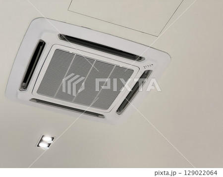 Modern cassette air conditioner unit on ceiling providing comfortable climate control. HVAC system offers cooling and ventilation for refreshing indoor atmosphere 129022064