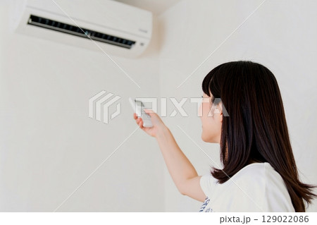 エアコンのリモコンで温度調整をする女性 129022086